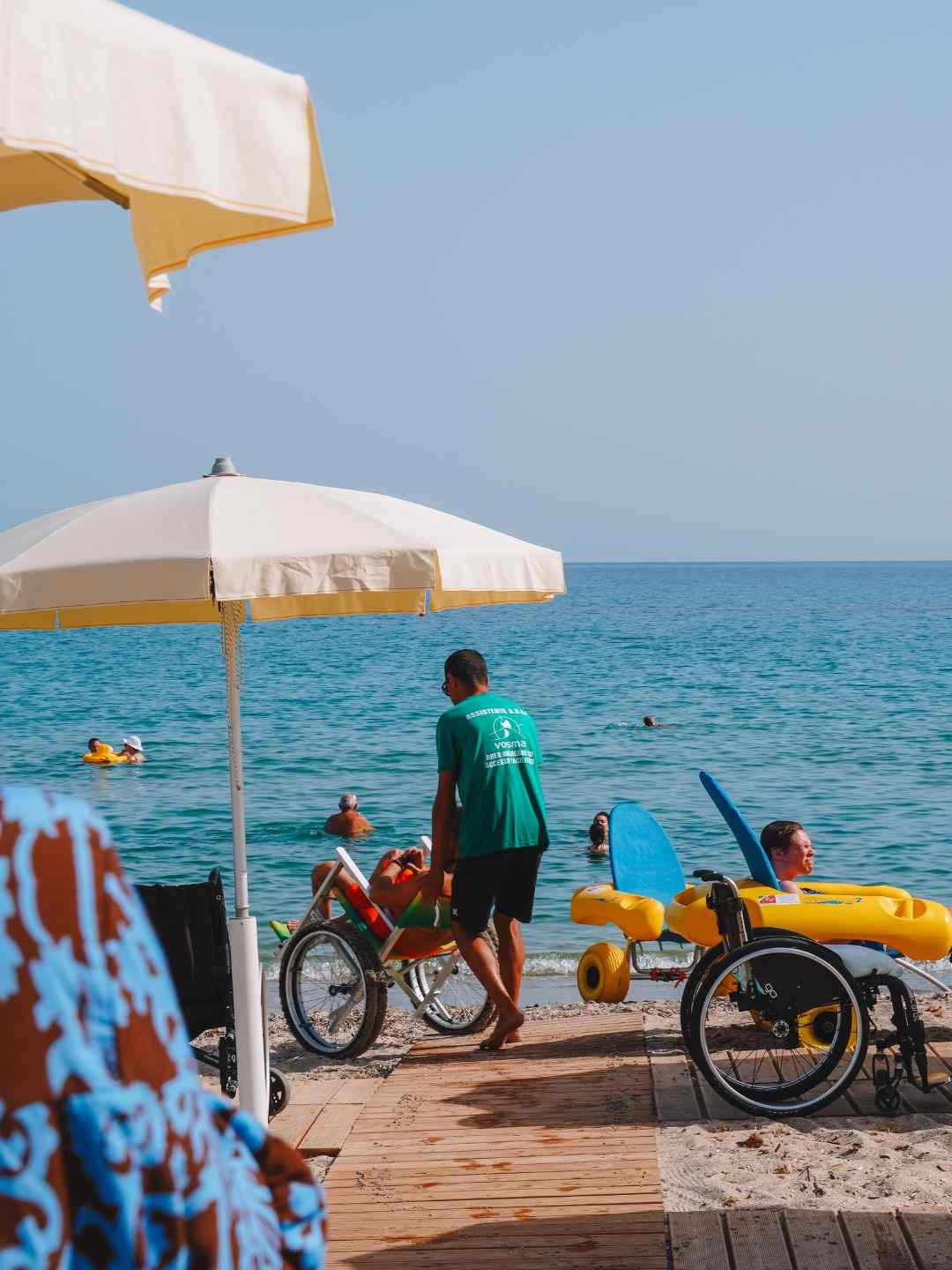 Assistente bagnino aiuta una persona con sedia job per l'accesso al mare sulla spiaggia di Platamona, Sassari